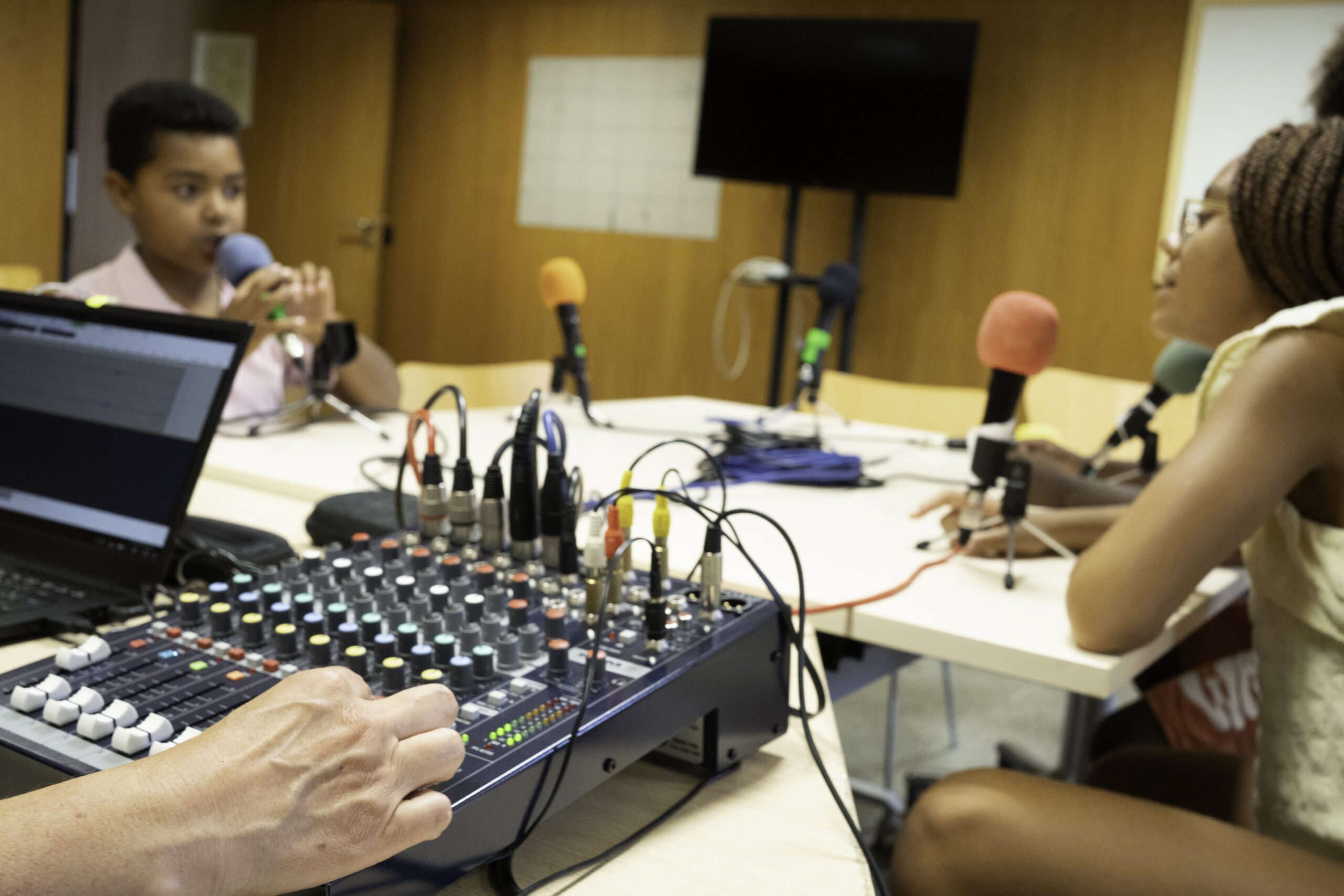 Afro children speaking into microphones, recording audio with a mixer and laptop in a studio setup